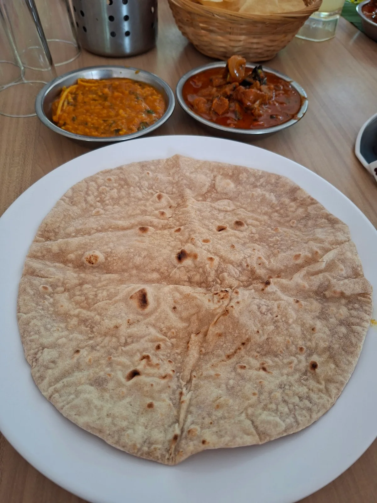 Chapati on a white plate with two metal bowls of curry behind it