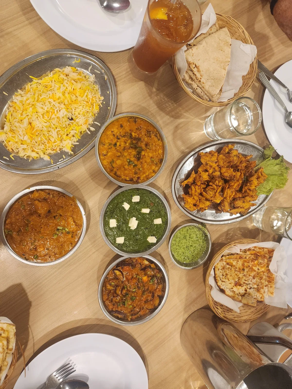 Overhead view of a table set with yellow rice, small metal bowls of curries, papadum and iced tea