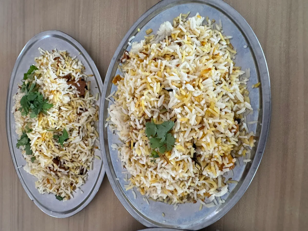 Two oval metal plates of biryani rice garnished with coriander
