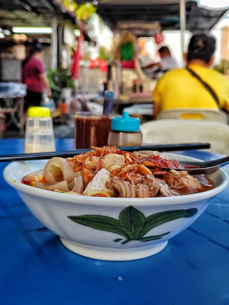 Bowl of hokkien mee with innards on a blue table outside the cafe