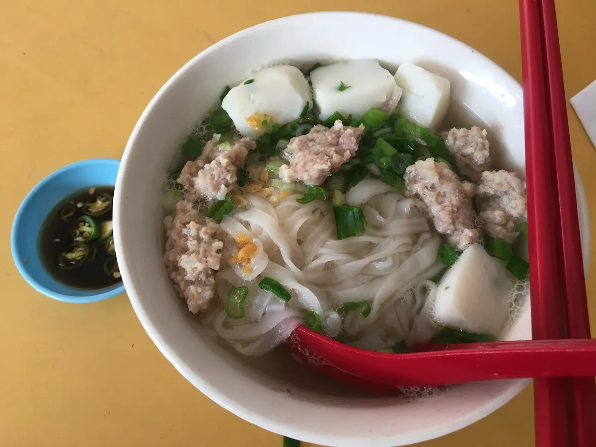 A bowl of noodle soup with minced pork, fish balls and tofu