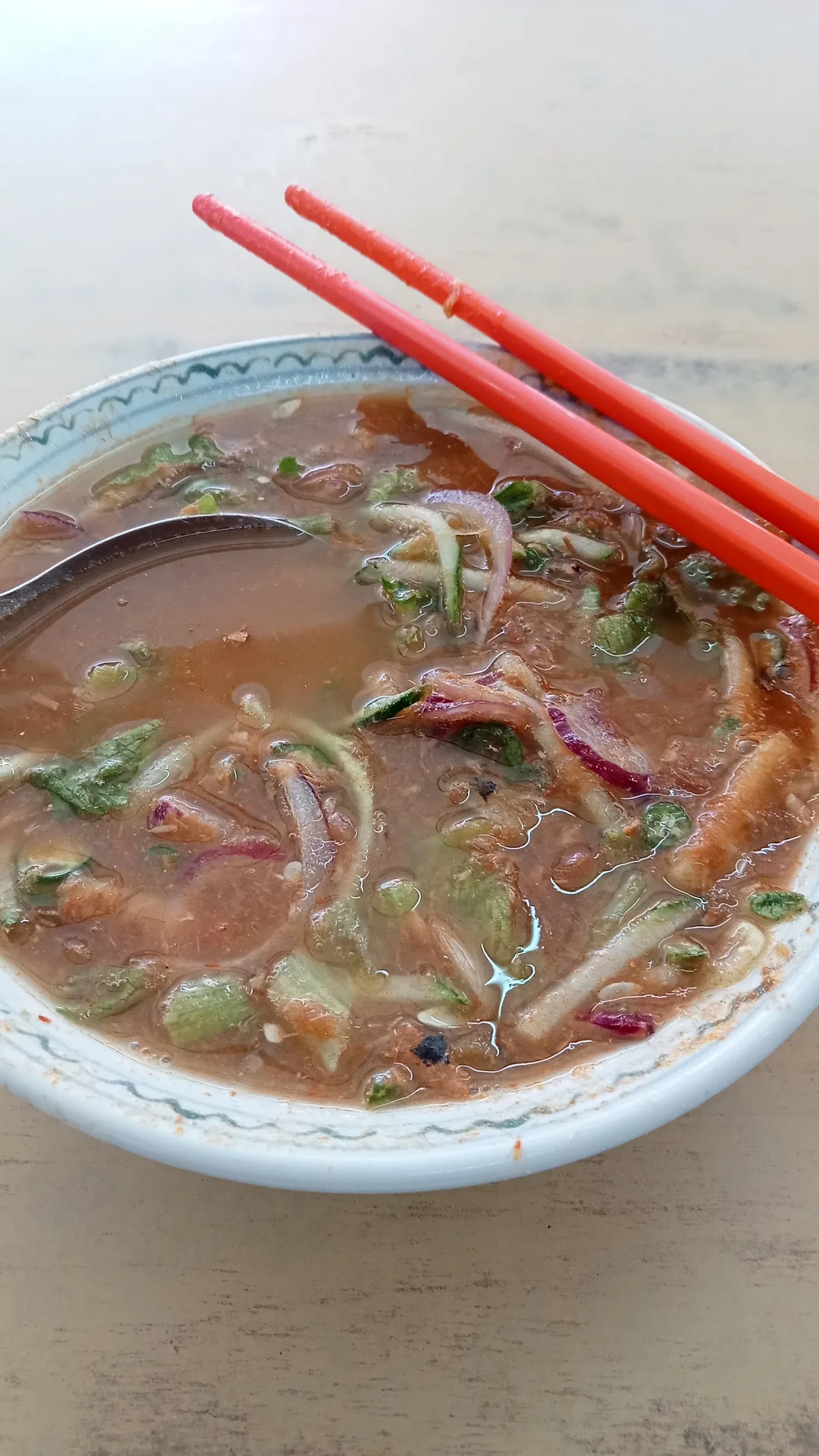 A bowl of noodles in a red-brown broth with sliced onion