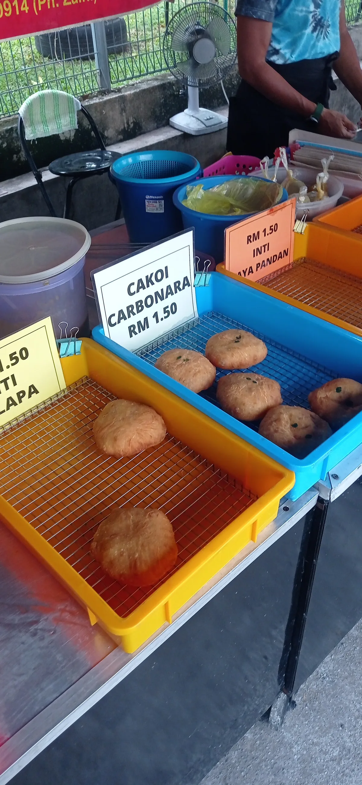 The roadside stall counter, coloured trays of freshly fried cakoi behind handwritten price cards