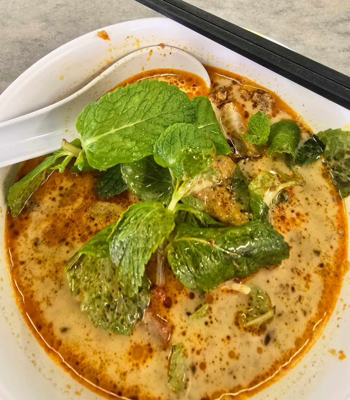 Curry mee in coconut-red broth heaped with mint leaves