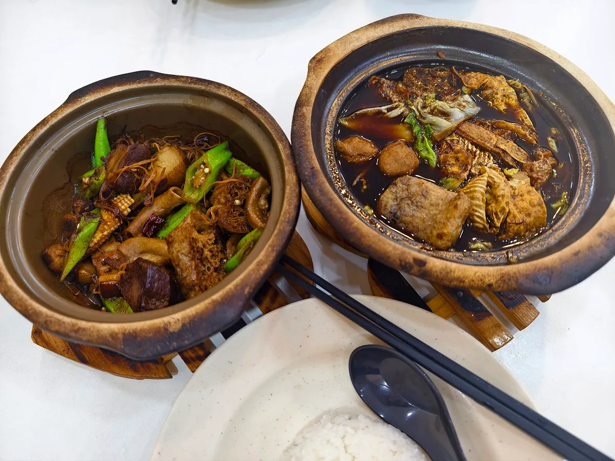 Two claypot dishes on wooden stands, with a plate of rice alongside