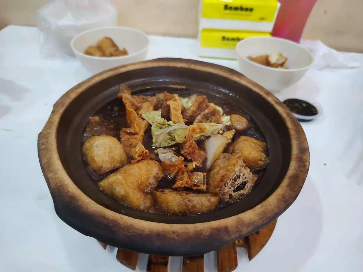 A claypot of braised fish balls, beancurd skin and cabbage on a wooden stand