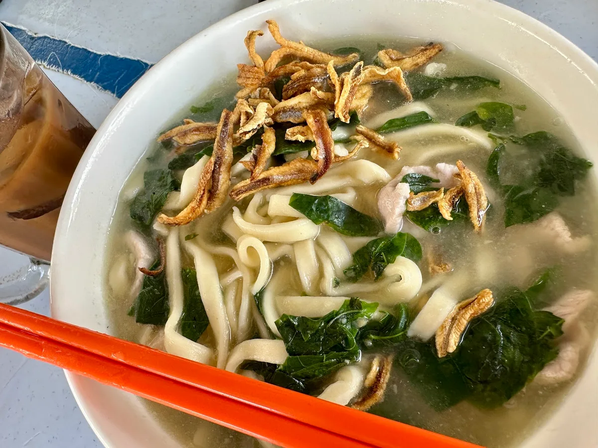 Soup ban mee heaped with fried anchovies, iced coffee alongside
