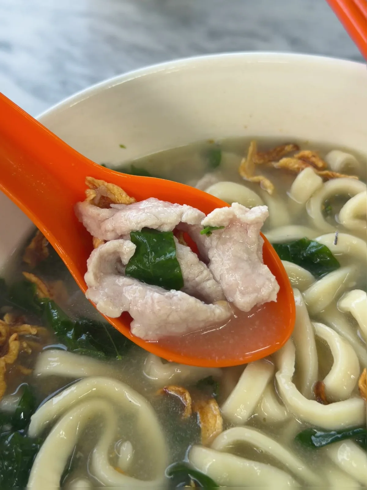 Spoonful of pork slices lifted from the ban mee soup