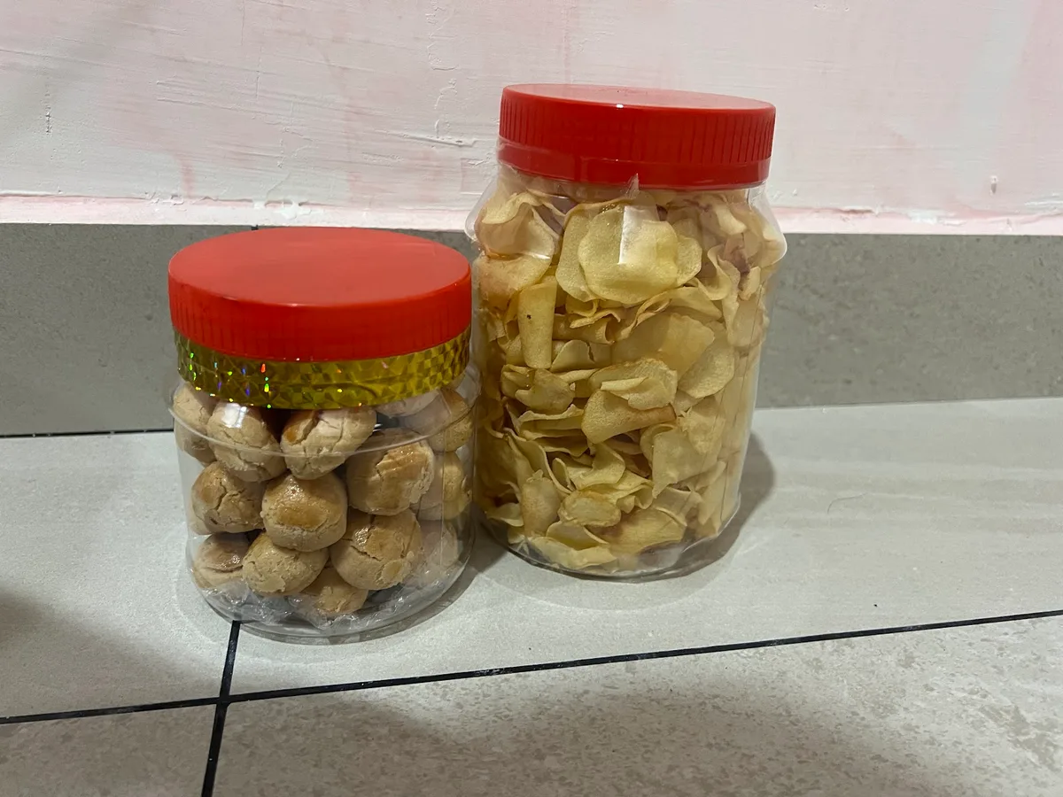 Two plastic jars with red lids holding biscuits and crackers on a tiled ledge