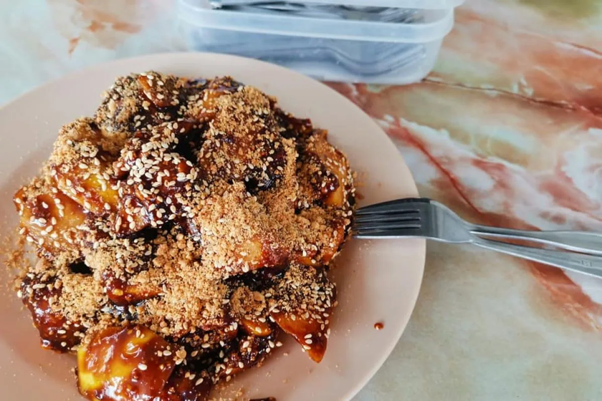 Plate of rojak in thick dark sauce under crushed peanuts and sesame seeds, fork resting on the plate