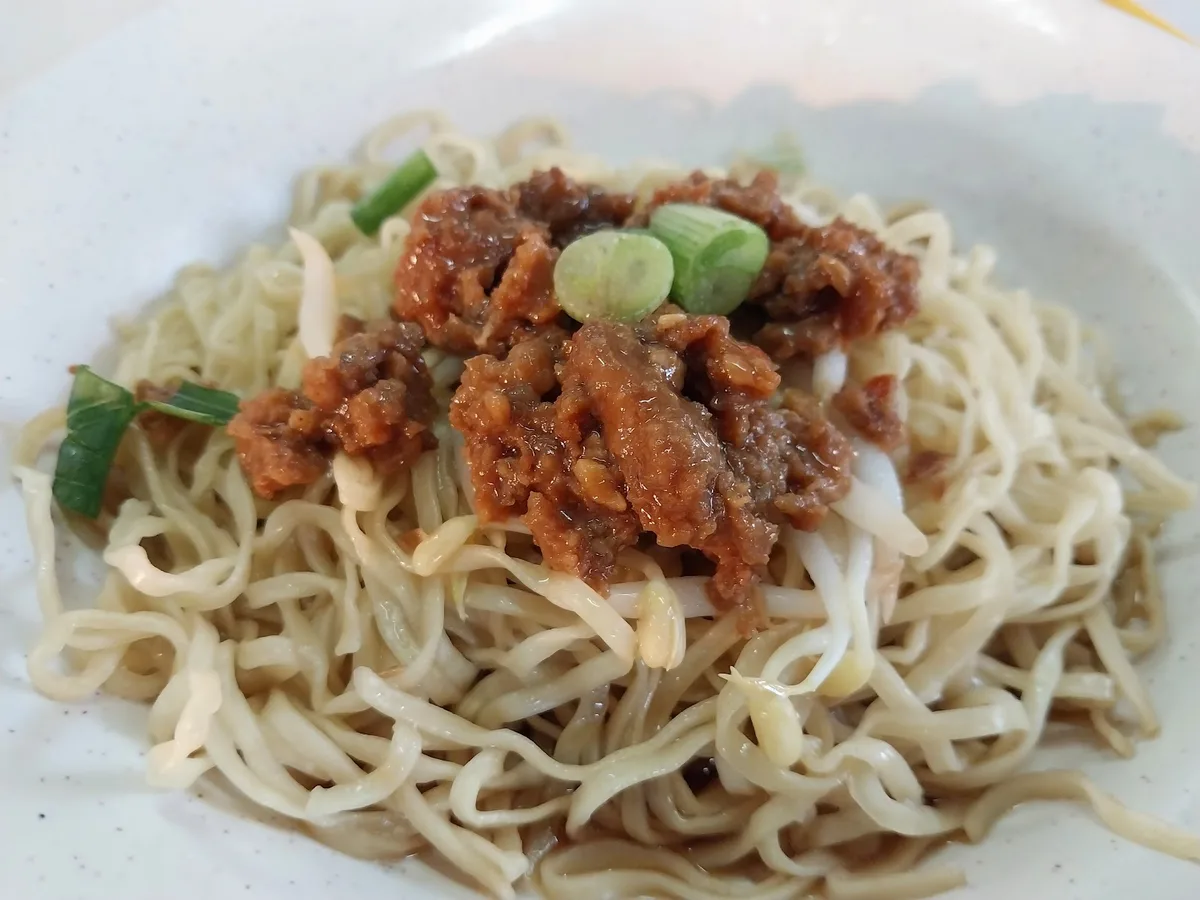 A plate of dry noodles topped with chilli sauce and green chilli