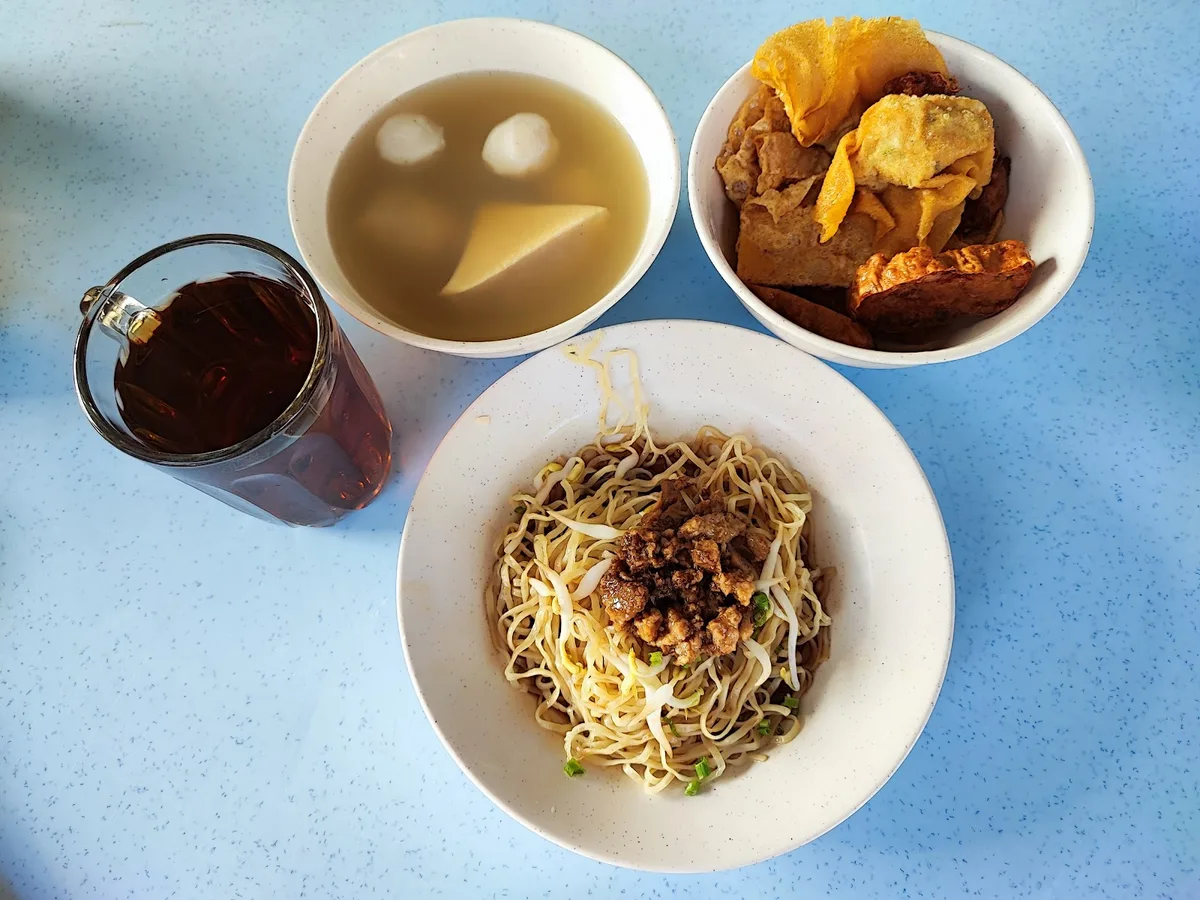 A set of dry noodles, fried yong tau foo and a glass of black coffee on the table