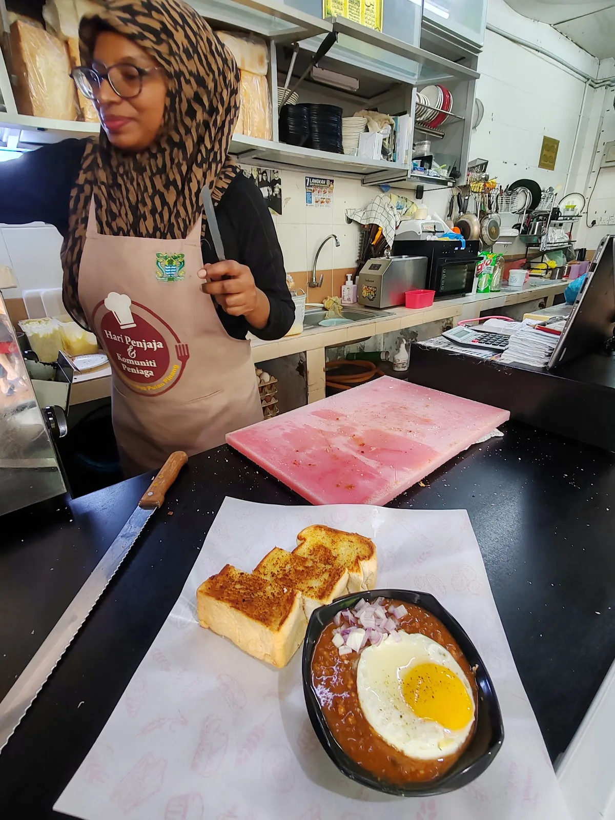 The cook in a Nazzeera's apron behind the counter