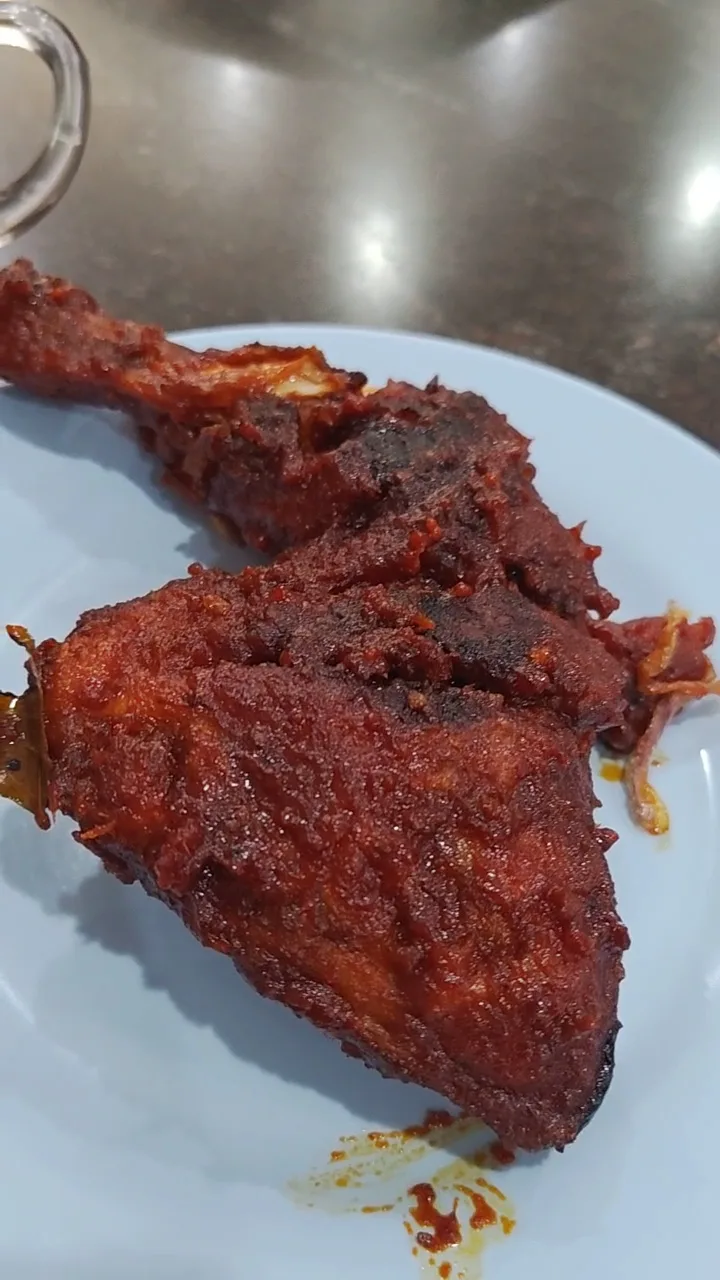 A piece of fried chicken coated in red spice on a white plate