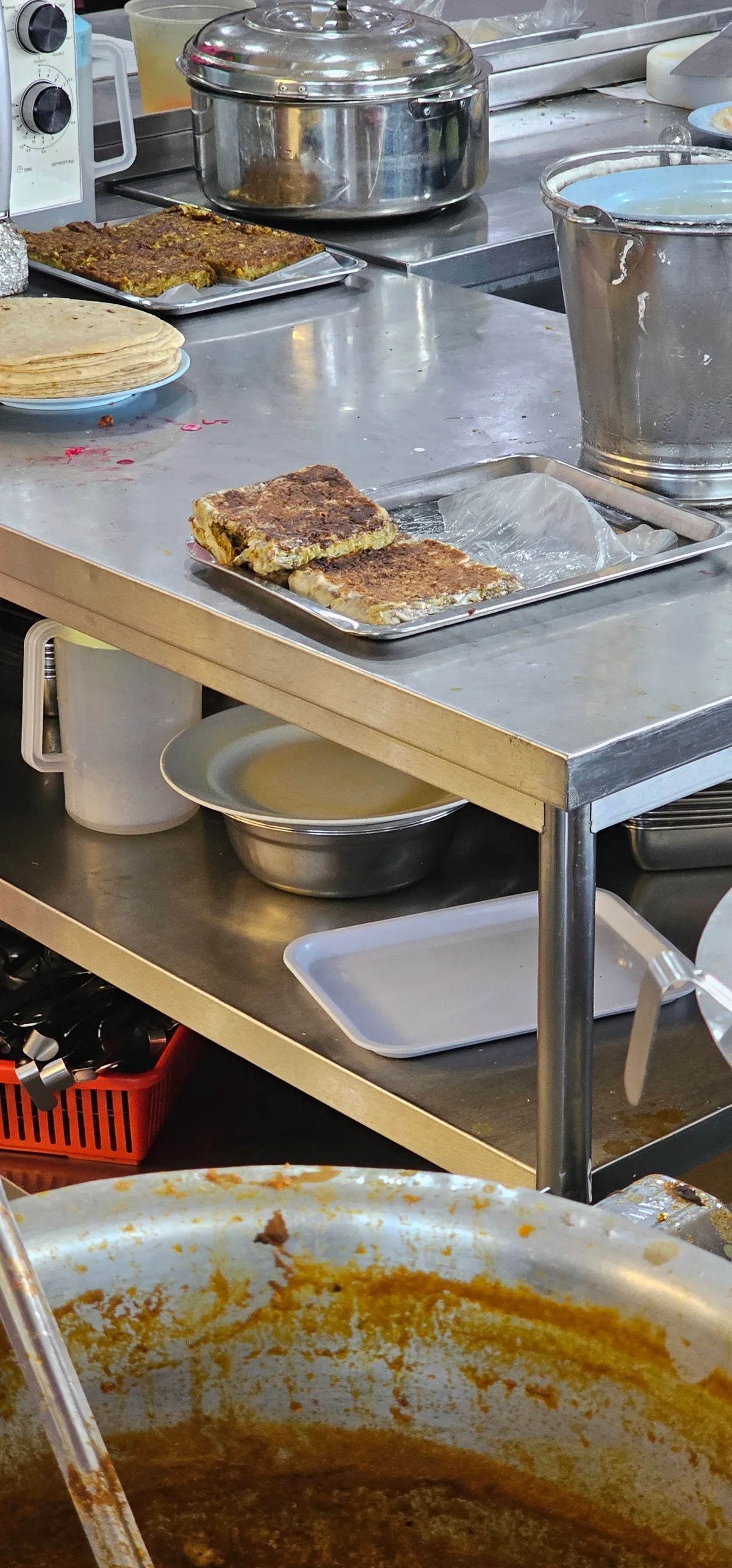 The prep counter with a tray of murtabak, stacked roti and steel pots