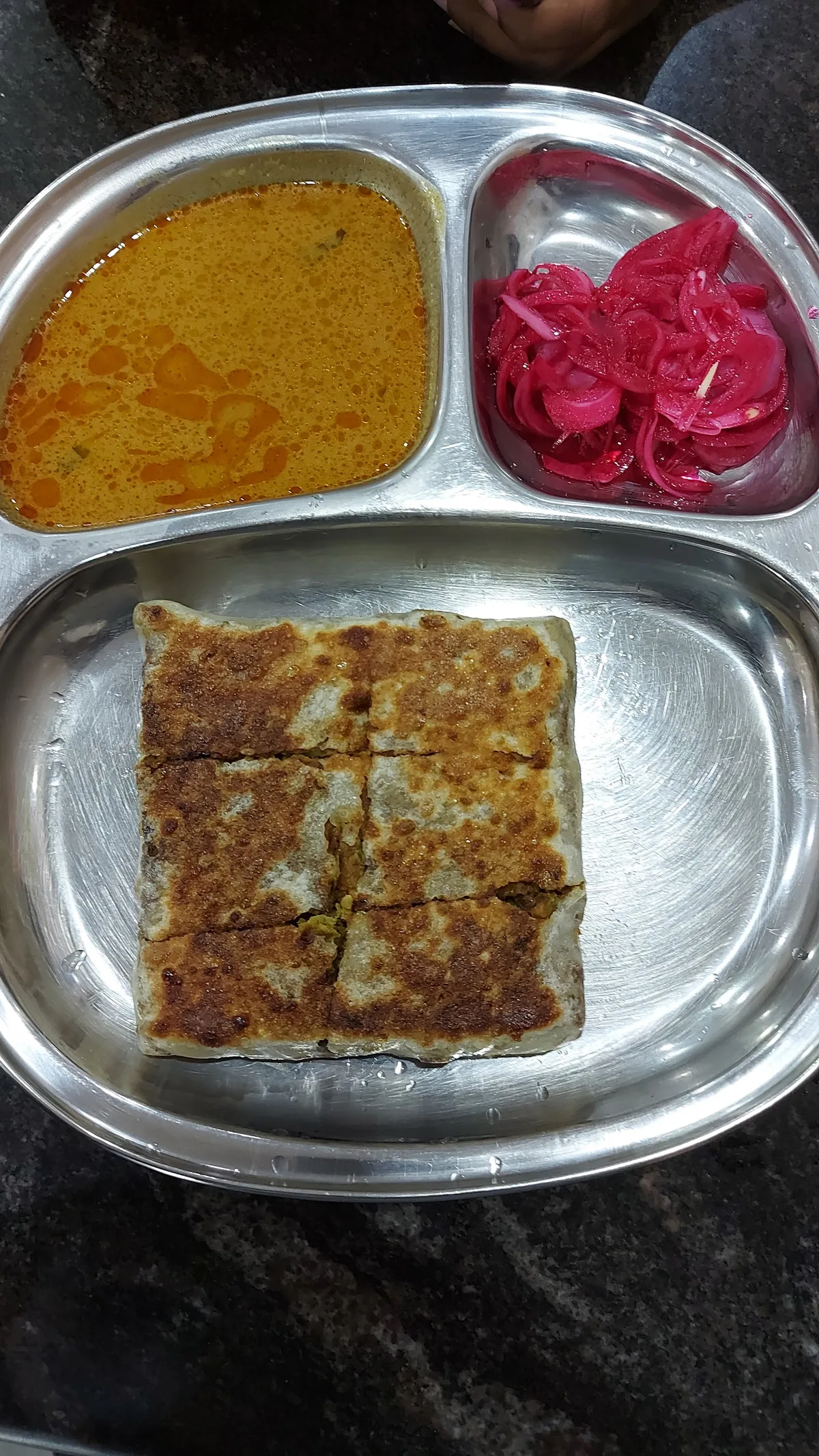Murtabak cut into squares on a steel tray with curry and pickled onions