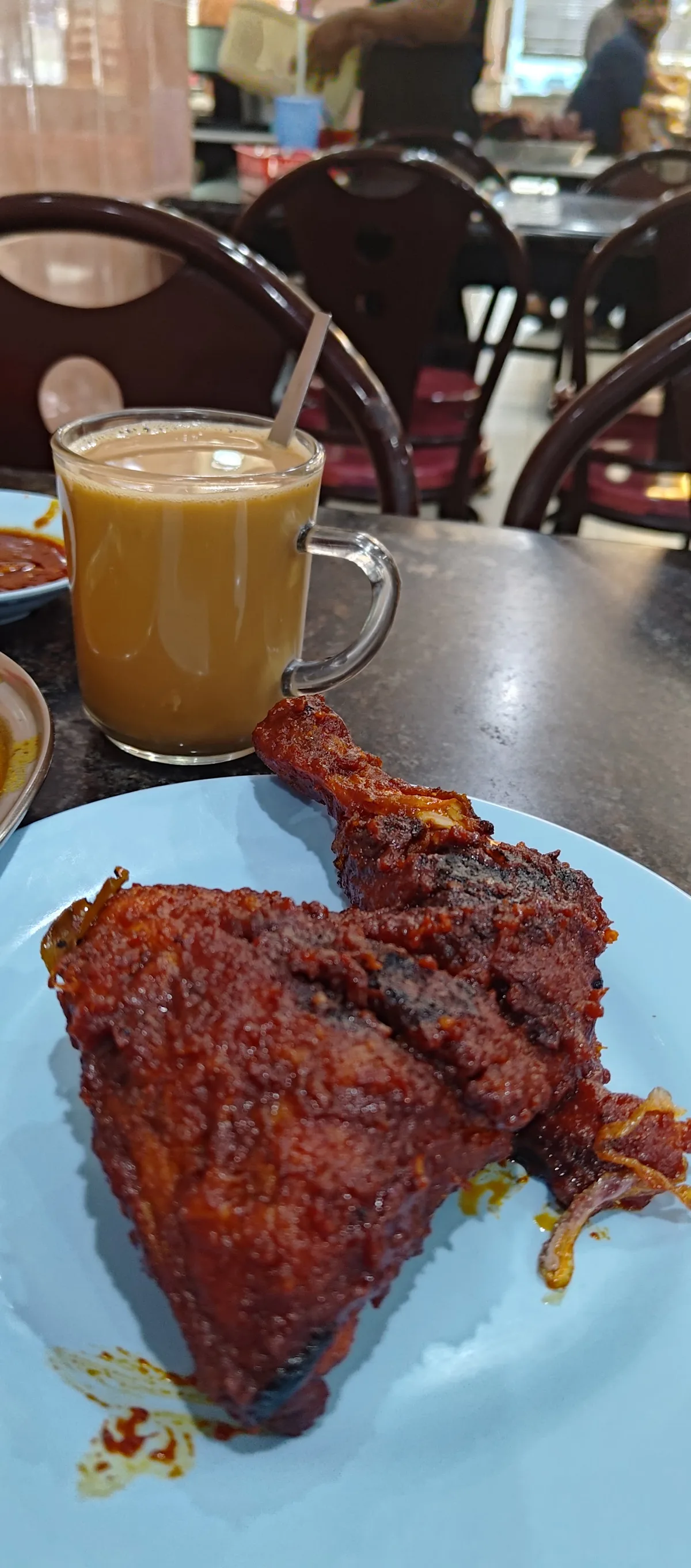 Fried chicken on a plate beside a glass of teh tarik in the dining room
