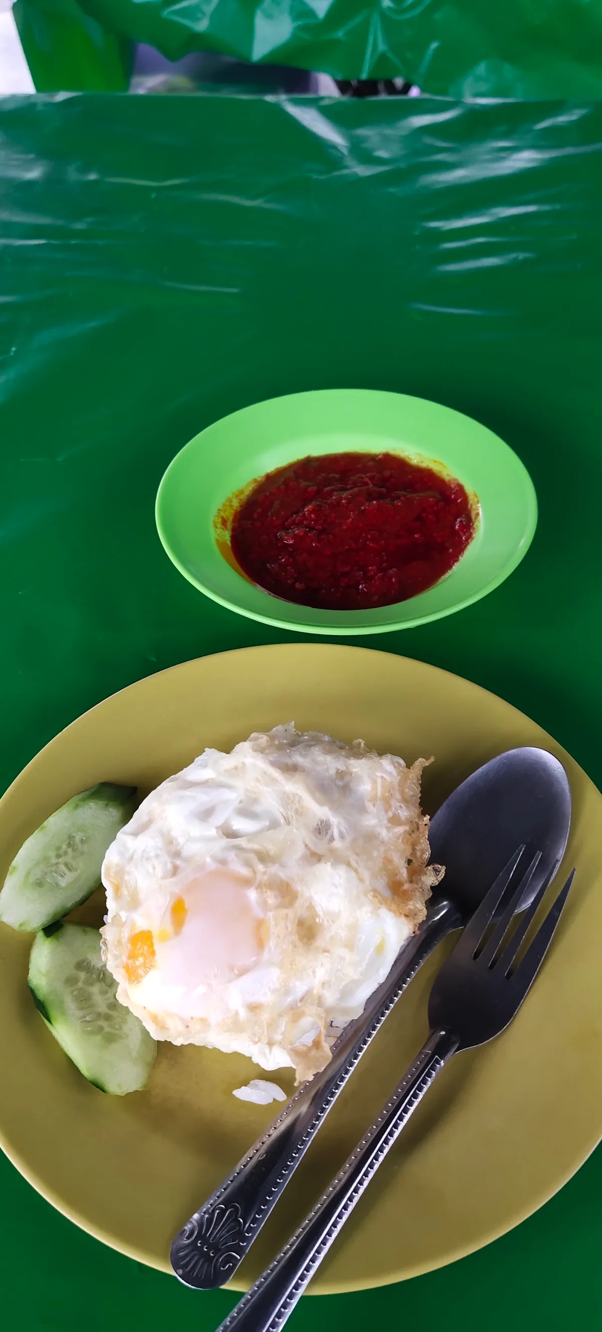 A fried egg over rice with cucumber and a dish of sambal