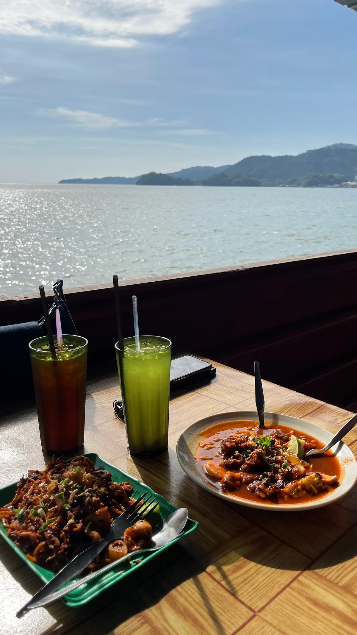 Mee rebus and drinks at a table over the sea