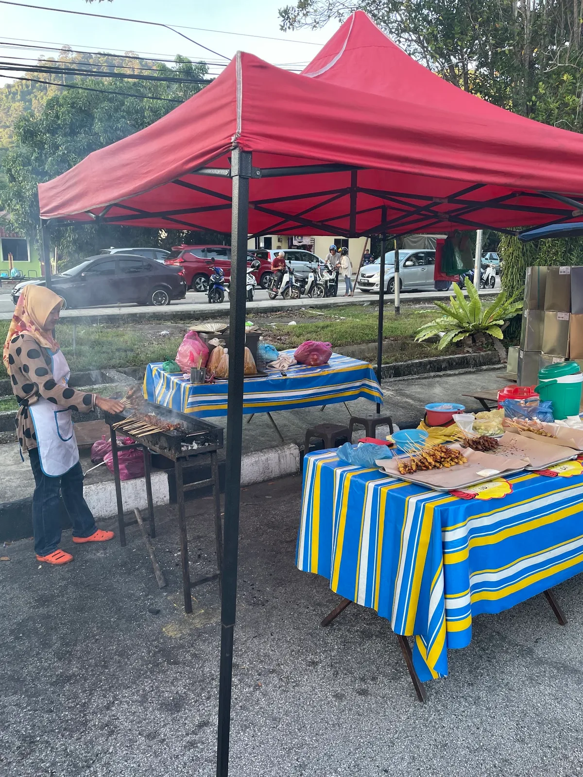 Satay stall grilling under a red canopy at the roadside market