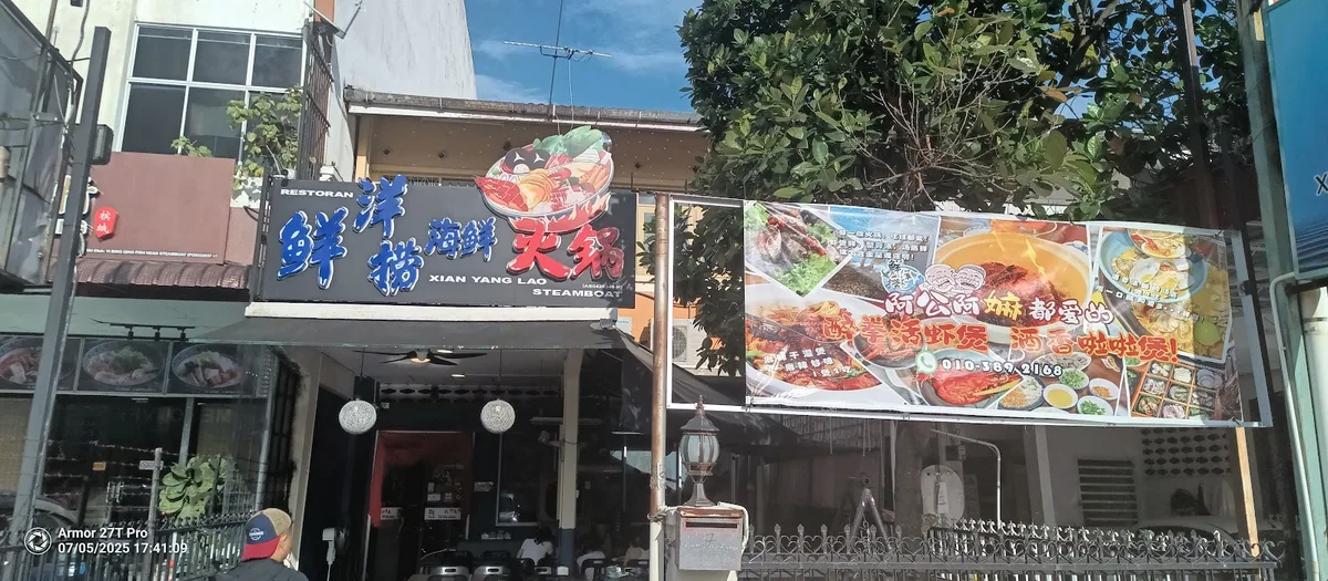 The Xian Yang Lao Steamboat signboard in Chinese and English above the shopfront awning, beside a banner of seafood photographs