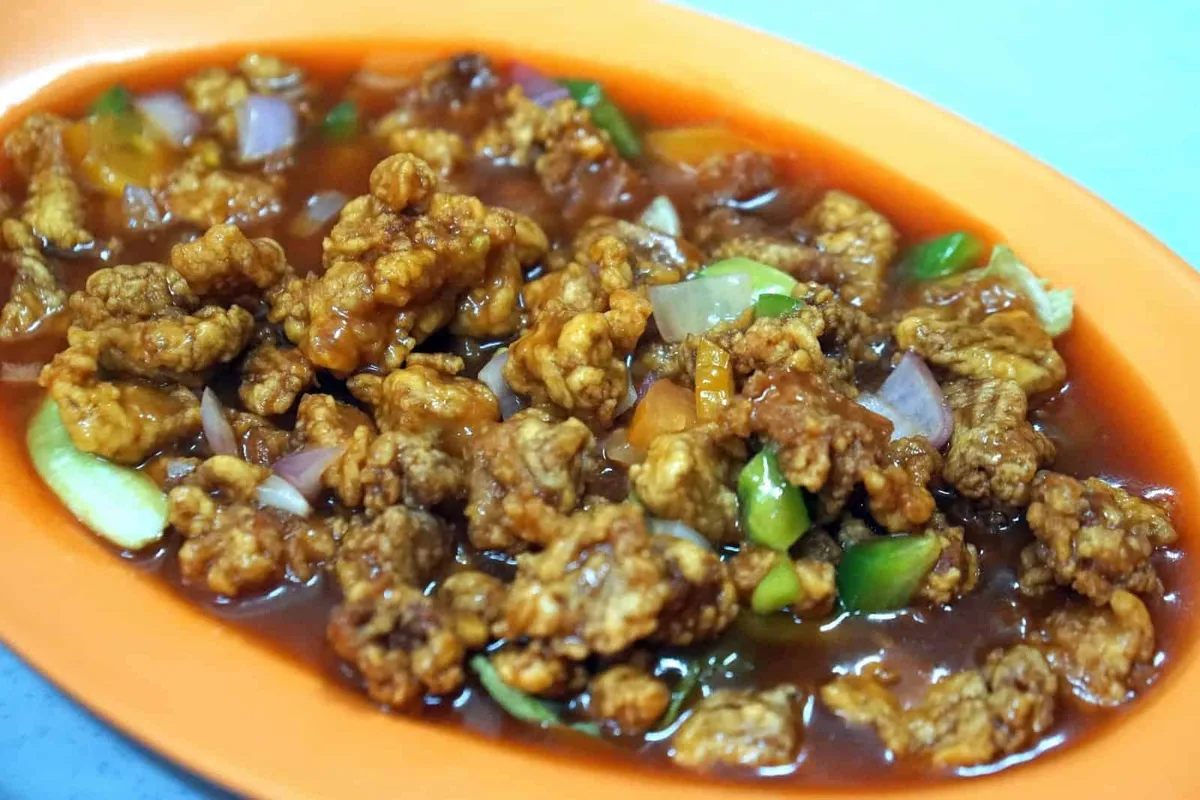 Battered fried meat in sweet and sour sauce with green capsicum, onion and tomato
