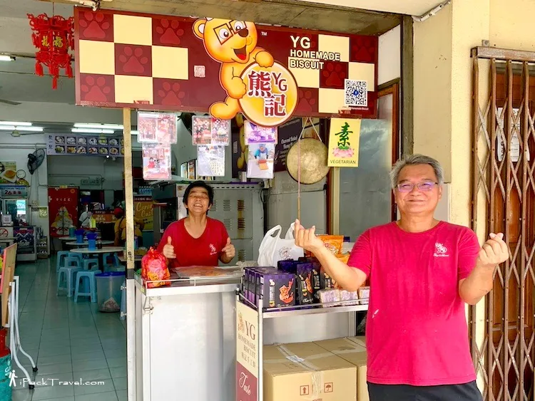 Shopfront counter under the YG Homemade Biscuit signboard with the owners standing beside the display